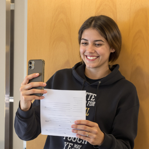 Young woman smiling while taking a photo of a tax form with her phone.